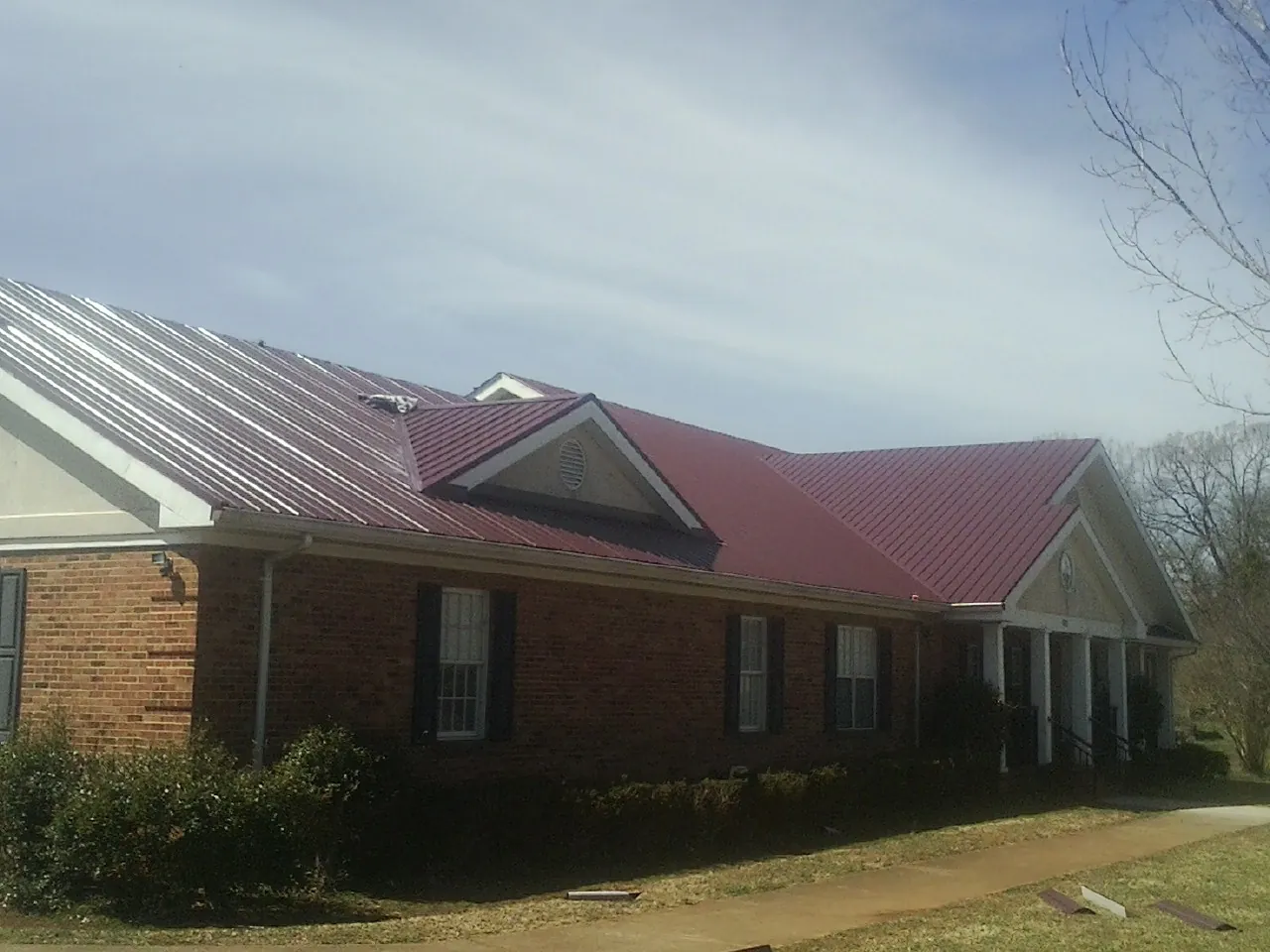 Red metal roof with gabled entries on a long brick building, from a Hail Damage Roof Repair job in Evansville